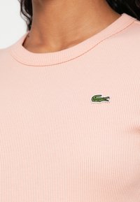 Jasnoróżowy prążkowany top z okrągłym dekoltem i haftowanym zielonym logo krokodyla na lewej piersi.