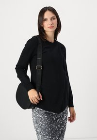 Maglione nero a maglia con collo rotondo, abbinato a una gonna argentata con paillettes e una borsa a tracolla nera rotonda con una tracolla logata.
