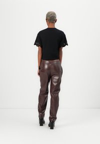 Black cropped shirt with scalloped sleeves and brown faux leather pants with pockets, featuring a high waist and straight leg design.