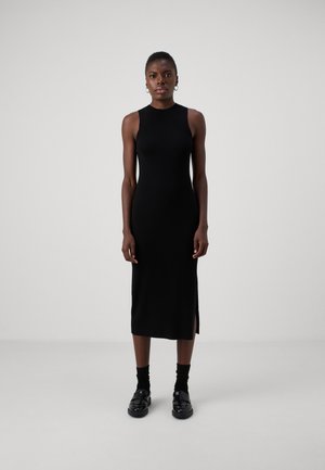 Black rib-knit midi dress with a sleeveless design and side slit. Model wears black platform shoes and ankle socks. Smooth texture.