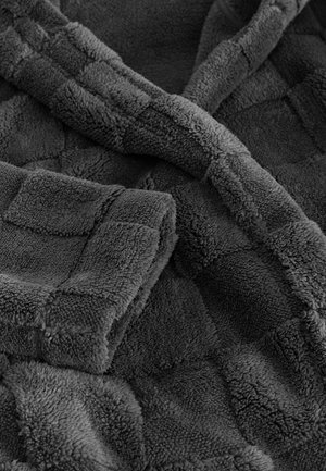 Grå plysstof tæt på med et ternet mønster, der viser en blød, tyk tekstur og foldede sektioner, hvilket fremhæver dets hyggelige udseende.