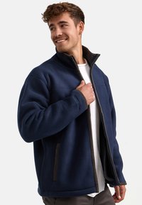 Dunkelblaue Fleecejacke mit hohem Kragen, Reißverschluss vorne und zwei seitlichen Taschen; verfügt über dunkelbraune Akzente und eine strukturierte Innenauskleidung.