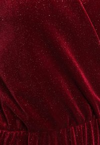 Tissu en velours cramoisi avec une texture douce, parsemé d'éclats scintillants, et une ceinture froncée, mettant en valeur une couleur riche et une sensation luxueuse.