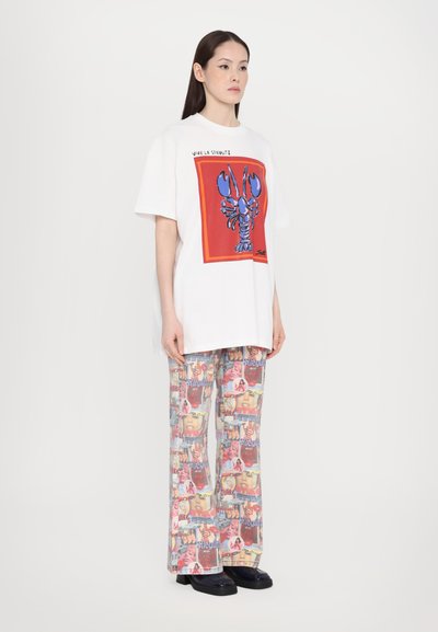 Balta per didelė t-shirt marškiniai su raudonos ir mėlynos spalvos omaro grafika, derinama su raštuotomis kelnėmis, vaizduojančiomis įvairius gyvenimus ryškiomis spalvomis.