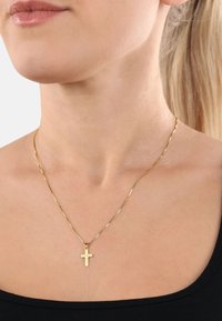 Goldener Kreuzanhänger an einer feinen, gedrehten Kette, auf nackter Haut liegend, präsentiert ein einfaches, minimalistisches Design.