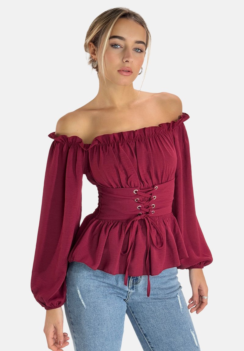Weinrote Bluse ohne Schulter mit Rüschensaum, langen Puffärmeln und einer taillierten Taille mit Schnürdetails. Kombiniert mit hochtaillierten Jeans.