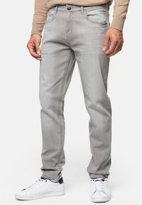 Jeans de mezclilla gris claro con corte recto, cinco bolsillos y detalles de costura sutiles, combinados con zapatillas blancas.