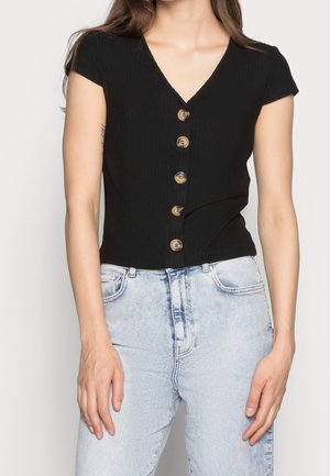 Zwart geribd kort mouwshirt met een V-hals en zes knopen in goudkleur aan de voorkant, gecombineerd met lichtblauwe high-waisted jeans.