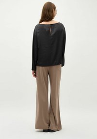 Sort bluse med lange ærmer og løs pasform, med en nøglehuldetalje på bagsiden, parret med beige, vidde bukser. Mat tekstur hele vejen igennem.