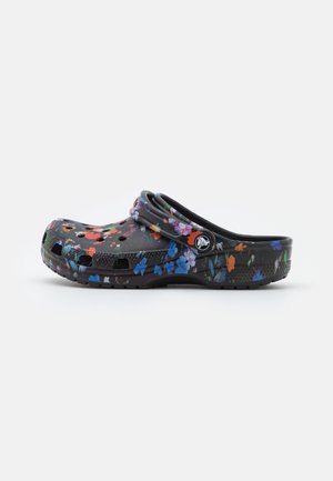 Sabot noir avec motif floral multicolore, trous de ventilation et bride de talon réglable avec bouton logo circulaire sur fond blanc.