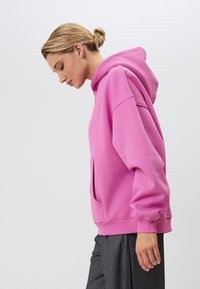 Liela rozā kapuce, izgatavota no mīkstas auduma, ar priekšējo kabatu, ribotām piedurknēm un kapuci, apvienota ar pelēkiem joslotiem biksēm.