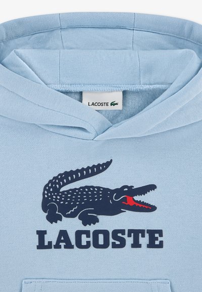 Светлосиня качулка с тъмносиньо и червено крокодилско лого и текст "LACOSTE", отпечатан под врата и маркова етикета отвътре до яката.