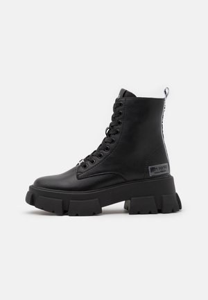 Schwarzer Leder-High-Top-Stiefel mit dicker, klobiger Sohle, Schnürung vorne und gebrandetem Zuglasche hinten vor weißem Hintergrund.
