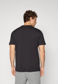 Zwarte T-shirt met korte mouwen van katoen, met een ronde hals en een ontspannen pasvorm, weergegeven van de achterkant tegen een lichtgrijze achtergrond.
