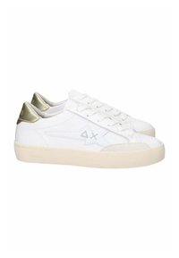 Weiße Leder-Sneaker mit strukturiertem Design, beiger Sohle und metallisch goldenen Akzenten an der Ferse. Mit flachen Schnürsenkeln und Branding.