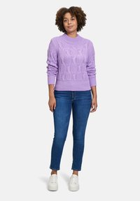 Lavenderfarbener Strickpullover mit einem groben Kabelmuster, rundem Ausschnitt und gerippten Bündchen. Kombiniert mit blauen engen Jeans und weißen Sneakers.
