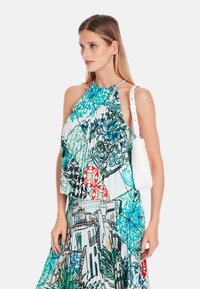 Halter neck dress in lightweight fabric, featuring colorful patterns of florals and architectural designs. White handbag with shoulder strap.
