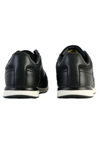 Sneaker in pelle nera con tacco arrotondato, cuciture a vista e suola in gomma bianca. La vista posteriore mette in evidenza il colletto imbottito e il tacco testurizzato.