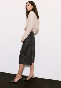 Pulover bej tricotat, culotte negre din piele, de lungime medie, și pantofi slingback negri din piele lucioasă. Textură netedă, formă ajustată, design minimalist.