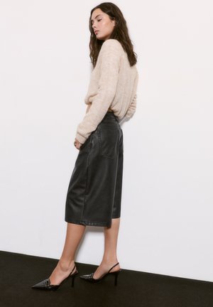 Bežani pleteni pulover, crne kožne culottes srednje dužine i crne patentne štikle na petu. Glatka tekstura, prilagođeni oblik, minimalistički dizajn.