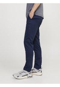 Mörkblå byxor i flexibel tyg, med slim fit, fickor och en mjuk yta, kombinerade med gråa träningsskor.