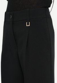 Melnas piegrieztas bikses ar elegantu dizainu, taisnstūra metāla akcentu uz jostasvietas un gludu audumu ar apdari.