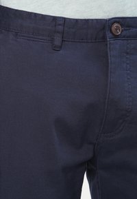 Navy blue chinos made from cotton fabric, featuring a button closure, belt loops, and subtle stitching details along the pockets.