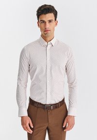 Biała koszula z długim rękawem w mały, kolorowy wzór w kropki. Połączona z brązowymi spodniami i pasującym paskiem. Gładka tekstura.