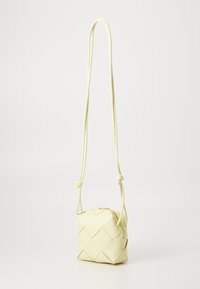 Light yellow woven leather crossbody bag with adjustable knot strap and gold zipper closure. Compact square shape with textured surface.
