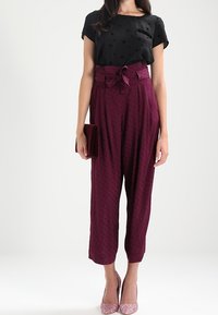 Top negro de manga corta con patrón de estrellas; pantalones burdeos de cintura alta con cinturón atado; tacones brillantes rosas; cartera roja.