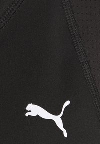 Tessuto atletico nero con una superficie testurizzata e bordi cuciti, caratterizzato da un logo Puma bianco in posizione di salto nell'angolo in basso a sinistra.
