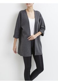 Grå vävd cardigan med lös passform, öppen front och trekvartsärmar. Bärs över en vit topp och matchas med svarta leggings.