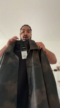 Svart läderjacka med krage, knappar framtill och en enda ficka. Har en sliten finish med en polerad textur. Hängande på en krok.