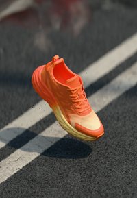 Sapatilha de corrida em gradiente de laranja a amarelo, com parte superior de malha respirável, sola texturizada para aderência e biqueira reforçada.