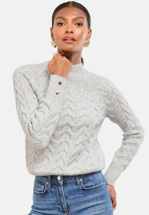Grau gestrickter Pullover mit geripptem Kragen und Bündchen, mit drei dekorativen Knöpfen am Ärmel, getragen über blauen Jeans.