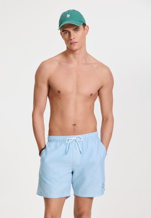 Blue-and-white striped swim shorts with elastic waistband and drawstring, paired with a green cap featuring a pink emblem.