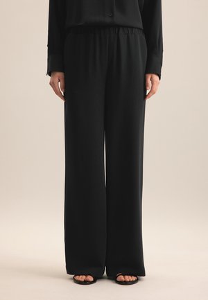 Pantalons larges noirs en tissu doux avec une taille élastique. Le tissu tombe doucement, créant une silhouette décontractée.