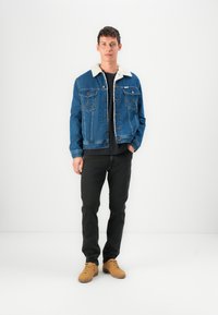Spijkerjack met een witte bontkraag, voorzien van twee borstzakken en knoopsluiting. Gecombineerd met zwarte jeans en tan sneakers.