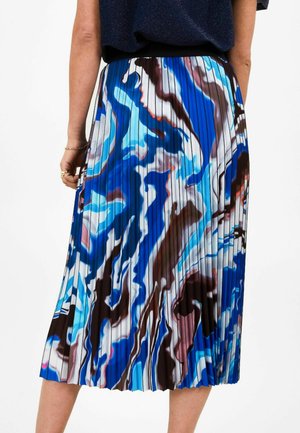 Woman wearing a pleated midi skirt with abstract blue, white, brown, and black swirl patterns, paired with a dark top.