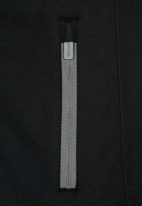 Zwarte stof met een gladde textuur met een verticale ritszak, omlijnd met een gestructureerd zilverkleurig materiaal, en een klein grijs logo.