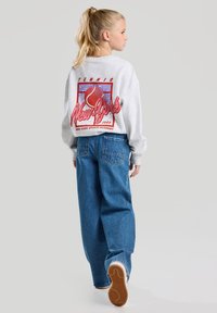 Gray sweatshirt featuring a retro red and blue graphic with a tennis ball, paired with loose-fit blue jeans and white sneakers.