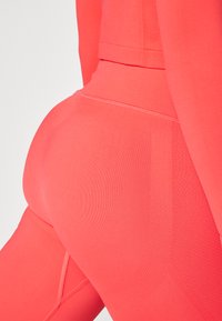 Høyt midjede treningstights i lys korall. Glatt, elastisk stoff med en tettsittende design og subtile sømdetaljer for forbedret fasong.