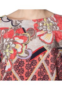 Top con estampado floral que presenta vibrantes tonos rojos, amarillos y morados sobre un fondo claro; escote redondo y acentos geométricos en el dobladillo.