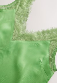 Green satin garment featuring lace trim along the neckline and armholes. Smooth texture with delicate floral lace patterns.