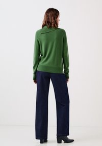 Maglione verde con una vestibilità leggermente oversize, con orlo e polsini a coste. Abbinato a jeans a gamba larga blu scuro e stivali neri alla caviglia.