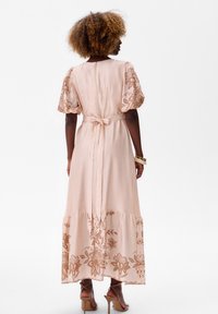 Maxi-jurkje in zachtroze stof met geborduurde bruine bloempatronen op de pofmouwen en de zoom, met een strikceintuur in de taille.