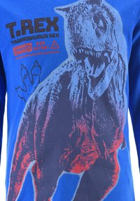 Long-sleeve blue t-shirt featuring a graphic of a T. rex in red and dark gray, with text “T.REX” and “HIGH VOLTAGE” in black.