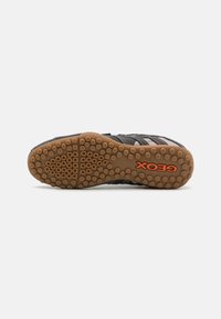 Black mesh sneaker with textured upper, reinforced sides, and a brown rubber sole featuring circular grip patterns. Orange "Geox" logo on heel.