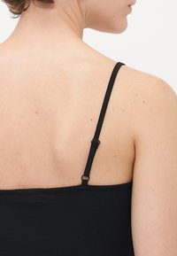 Gros plan sur le haut du dos et l'épaule d'une personne portant un top noir à bretelles spaghetti avec une boucle de réglage.