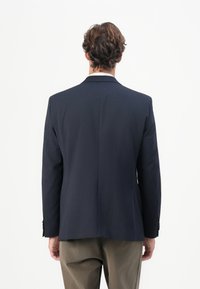 Temno modra blazer s krojenim krojem, enim razporkom in strukturiranimi rameni. Ima gumbaste manšete in gladko teksturo.